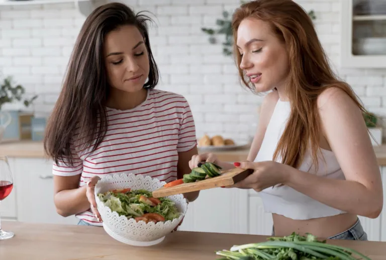 Mujeres compartiendo alimentos saludables en una mesa con frutas, verduras y productos nutritivos, tal como lo plantea Grupo Kosmos.