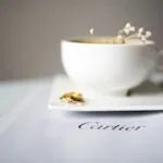 Anillos de oro junto a una taza de café sobre una publicación de Cartier, imagen que representa el legado de Cartier Women’s Initiative y su apoyo al liderazgo femenino.