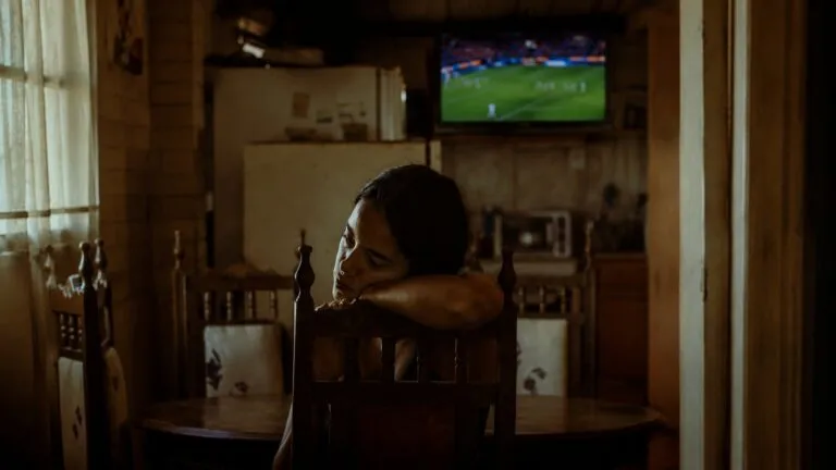 Mujer sentada en una mesa de comedor mientras observa a la distancia una televisión con un partido de fútbol durante el Mundial 2026, imagen utilizada para ilustrar la campaña de prevención de la violencia familiar impulsada por ONU Mujeres, Unicef y UNFPA en México.