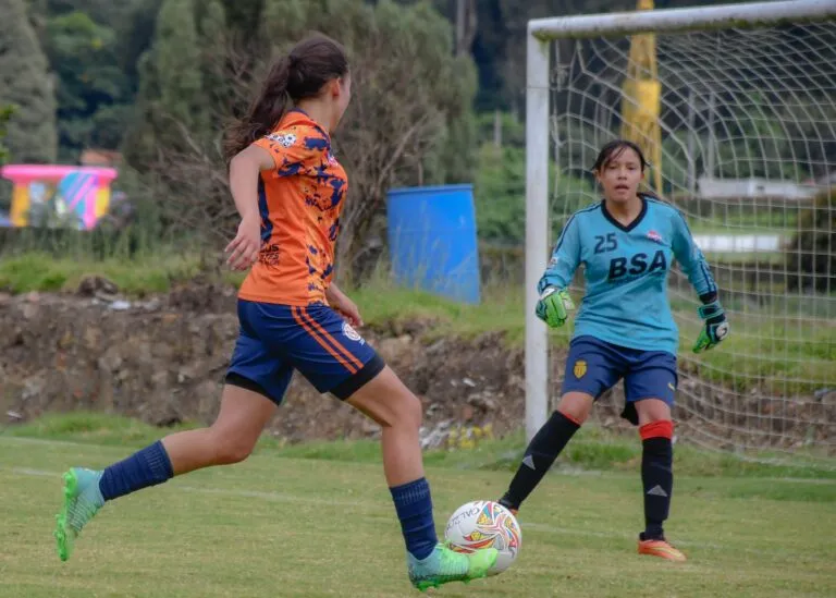 Dos jóvenes futbolistas disputan una jugada durante un partido de futbol femenil en una cancha comunitaria.