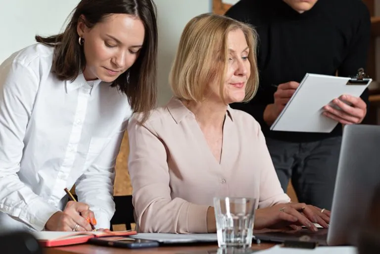 Dos mujeres profesionales trabajan juntas frente a una computadora en una oficina, reflejando el crecimiento del liderazgo femenino en los negocios y los desafíos que aún enfrentan para acceder a financiamiento empresarial.