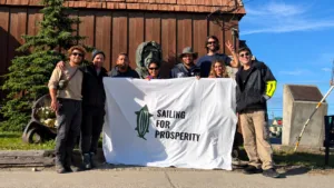     Integrantes de Sailing for Prosperity posan con la bandera de la expedición frente a un edificio de madera.