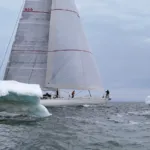 Velero Diablesse de Sailing for Prosperity navega entre dos bloques de hielo con sus velas desplegadas.