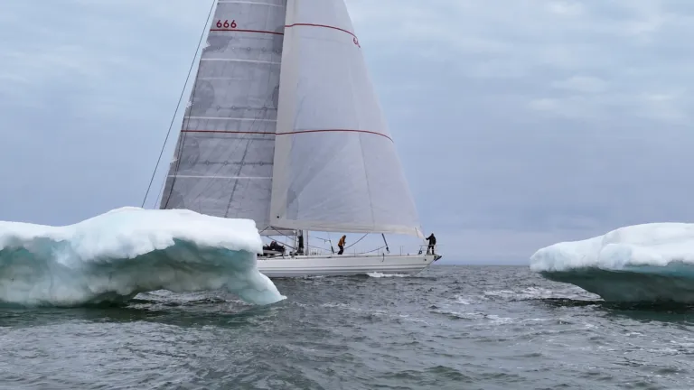 Velero Diablesse de Sailing for Prosperity navega entre dos bloques de hielo con sus velas desplegadas.